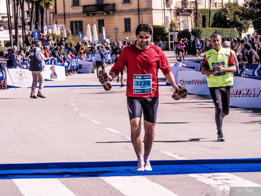Hurting Feet at Lago Maggiore Marathon, man crossing finish line with shoes in hand