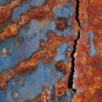 Colorfully rusty steel in blue, orange and rusty coloration and a crack in the steel.